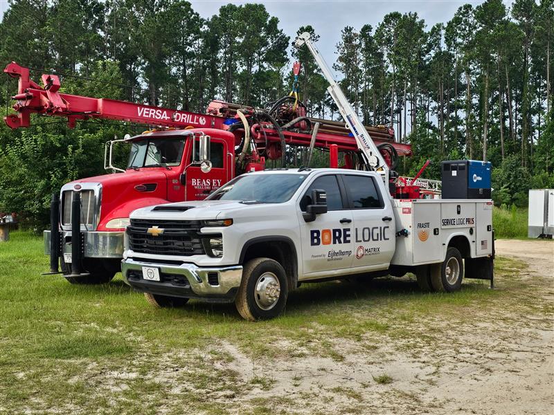 Bore Logic service truck parked beside a red Versa-Drill rig in a grassy field, showcasing on-site maintenance and drilling service capabilities.